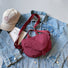 Flat lay of the burgundy nylon bag on a denim jacket, showing its vibrant outdoor style.