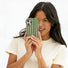 Model holding the green candy-striped wavy phone case to her face.