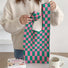 Model holding a vibrant pink and green checkered woven tote bag.