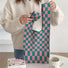 Model holding the pink and green checkered woven tote bag, showing its playful chic.