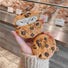 Model Hands holding two Chocolate Cookies  airpods cases, one closed and one open.