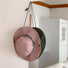 The pink version of the bucket hat hanging on a wall hook.