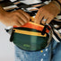 A close-up of a model holding a green and orange belt bag, emphasizing its compact size and easy access.