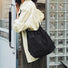 Black nylon drawstring bag with outer pockets, worn by a person in a striped shirt.