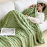 Model resting with green wave textured fleece blanket in living room, comfy lifestyle view.