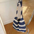 Close-up of Crochet straw tote bag with blue and natural-toned stripes, hanging from a chrome rail, ideal for errands.