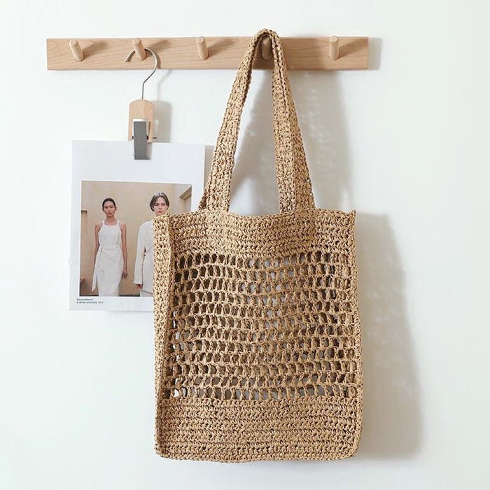 Light brown crochet straw tote bag with open weave design, hanging on a wooden rack.