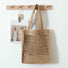 Light brown crochet straw tote bag with open weave design, hanging on a wooden rack.