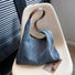 Angled view of dark blue denim shoulder bag with a diamond pattern and brown leather strap.