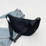 Black nylon crescent crossbody bag with adjustable strap and zip-top fastening, resting on a denim jacket.