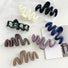 Flat lay of seven acrylic wave hair claws in black, cream, dark khaki, green, navy blue, brown, purple.