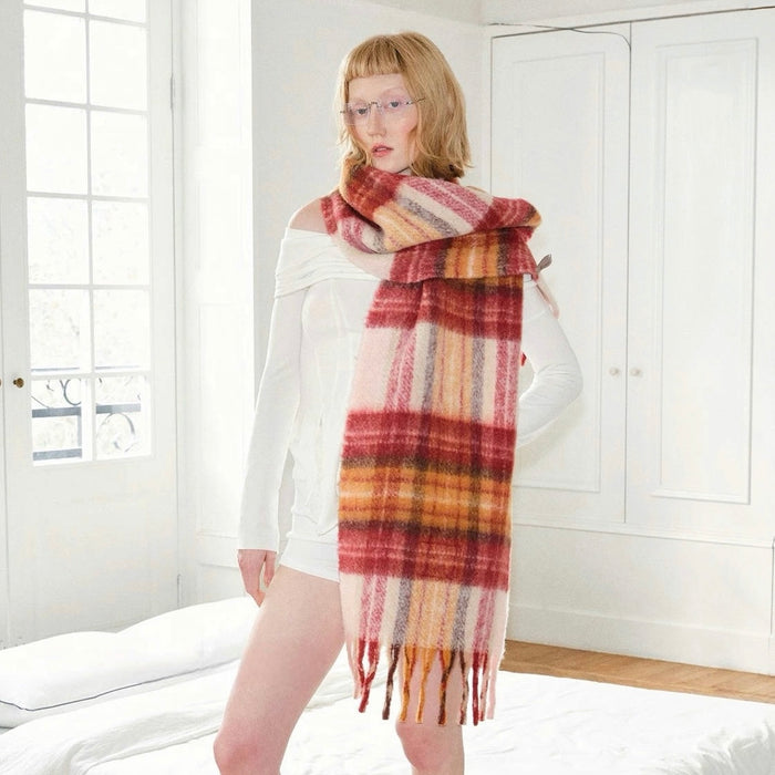 Woman wearing a long, wool blend Fiery Sunrise Plaid Scarf in red, orange, and pink tones with fringe.