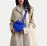 Klein blue padded nylon bag worn as a crossbody with a beige trench coat, showcasing the innovative strap design.