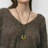 Model styling gold fluid oval pendant necklace with brown knitwear, minimalist aesthetic view