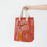 Red polyester mesh shopper bag with googly eyes, beige shoulder straps, holding snacks.