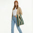 A woman  holding a green khaki stripe woven tote bag, highlighting the hands-free utility.