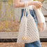 White hollow crochet tote bag made from cotton rope, held by a person outdoors.