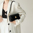 Black PU leather arc baguette shoulder bag with gold hardware, held by a person in a white blazer.