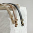 Close-up of three Linked Loop Belts in brown, black, and khaki, showing the gold-tone buckle detail .
