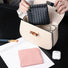 Hands holding black magnetic self-closing storage bag above handbag; woven-texture pouch for makeup and essentials.