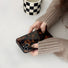 Hand in beige sweater holding Maillard Amber case. Warm tortoiseshell finish for cozy autumn fashion.