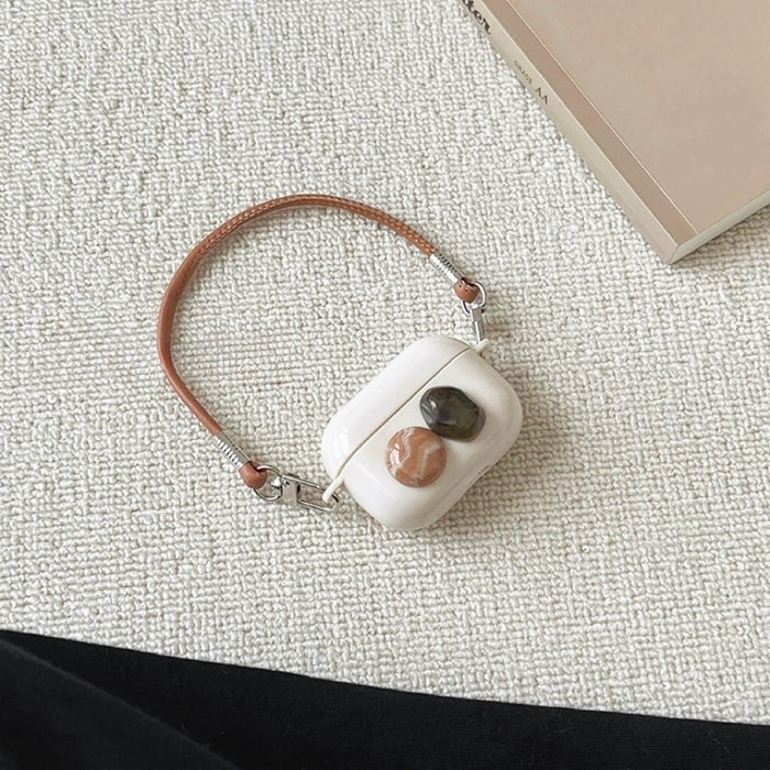 Front view of White silicone AirPods case with two Maillard color stone accents and a brown leather wrist strap.