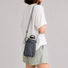 Back view of a model showcasing how the dark grey nylon bottle sling bag sits comfortably flat against the lower back.