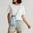 Model styling the light pastel blue nylon water bottle carrier bag over the shoulder with a basic white tee.