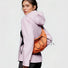 A model wearing an orange nylon crescent bag as a back-slung crossbody for outdoor adventure styling.