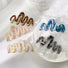 Front view of Four painted wave hair claws in brown, blue, pink, white, and black.