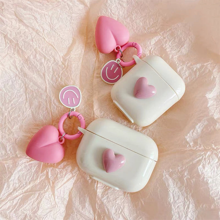 Two white silicone AirPods cases with pink heart charms and smiley face keychains.