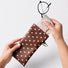 Close-up of hands pulling out the attached soft velvet wiping cloth from inside the brown polka dot sunglass case.