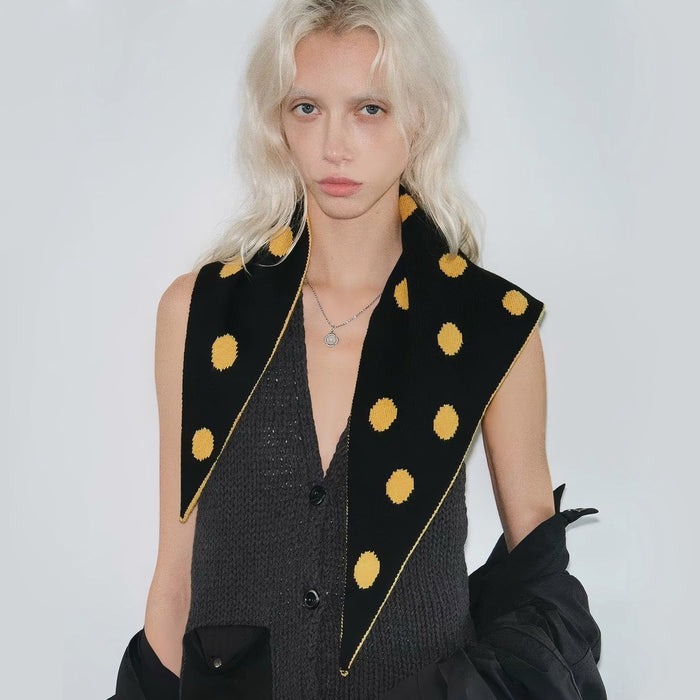 Model wearing black and yellow reversible polka dot knit triangle scarf.