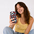 A smiling model in a crochet top taking a mirror selfie with the brown and blue polka dot iPhone case.