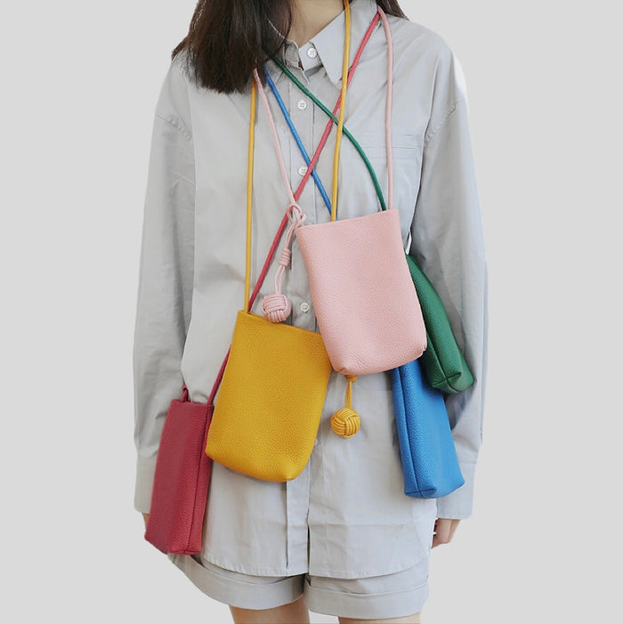 Fi ve Polycolor hanging ball leather bags in red,  pink, blue, green and yellow, worn together by a person.