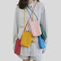 Fi ve Polycolor hanging ball leather bags in red,  pink, blue, green and yellow, worn together by a person.