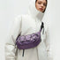 A women wearing a lilac purple technical nylon sling bag as crossbody, showcasing its sleek crescent silhouette and water-resistant fabric.