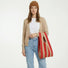 A woman holding a retro red and khaki stripe woven tote bag, showcasing its lightweight and effortless chic.