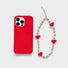 Red silicone case with a rainbow heart charm made of acrylic beads. Playful handcrafted jewelry style.