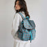 Side profile view of a model in a white sweatshirt carrying the blue plaid nylon laptop backpack.