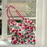 Angled view of Polyester Rose Romance Tote Bag with red rose print, red grab straps, hanging in a window.