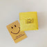 Foldable yellow oxford cloth shopper bag with a smiley face tag, beside a matching Smile to life card.