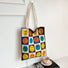 Flat lay of Knitted tote bag with colorful plaid smiley face design and cream straps in brown.