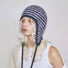 Model wearing a pink and dark grey striped knit earflap hat with braided tassel ties.