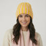 Model wearing Striped Fluffy Knit Beanie in yellow pink. Cheerful winter colors with high-density warmth.