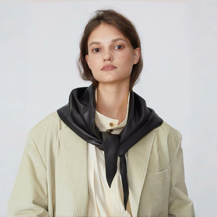 Close-up view of a model styling a black leather triangle scarf with a front knot.