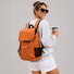 Model wearing the burnt orange flap commuter backpack outdoors.