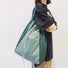 A model carrying the green 2-way bag as a shoulder tote, highlighting the durable handles and sleek profile.