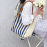 Model carrying a Vertical Striped Straw Tote Bag in blue, great for daily carry and travel.