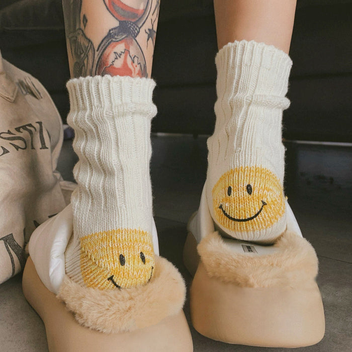 White socks with smiley face design worn with beige slippers on a blurred background